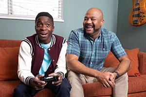 Adolescente con un control de videojuegos sentado en un sillón con un hombre.